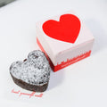 Heart-shaped brownie dusted with icing sugar beside its red heart gift box