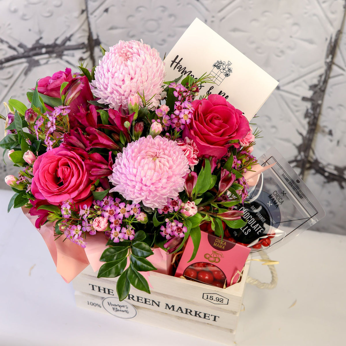 View from above of pink blooms and chocolates arranged in a white timber crate