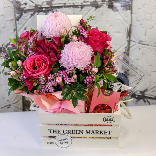 Front view of pink blooms and two chocolate packages arranged in a white timber crate