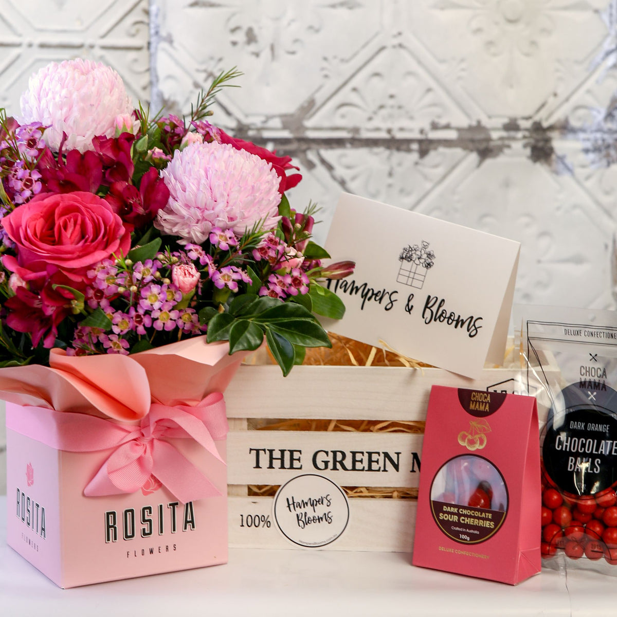 Pink floral pot and two chocolate packages displayed beside a white crate with a message card