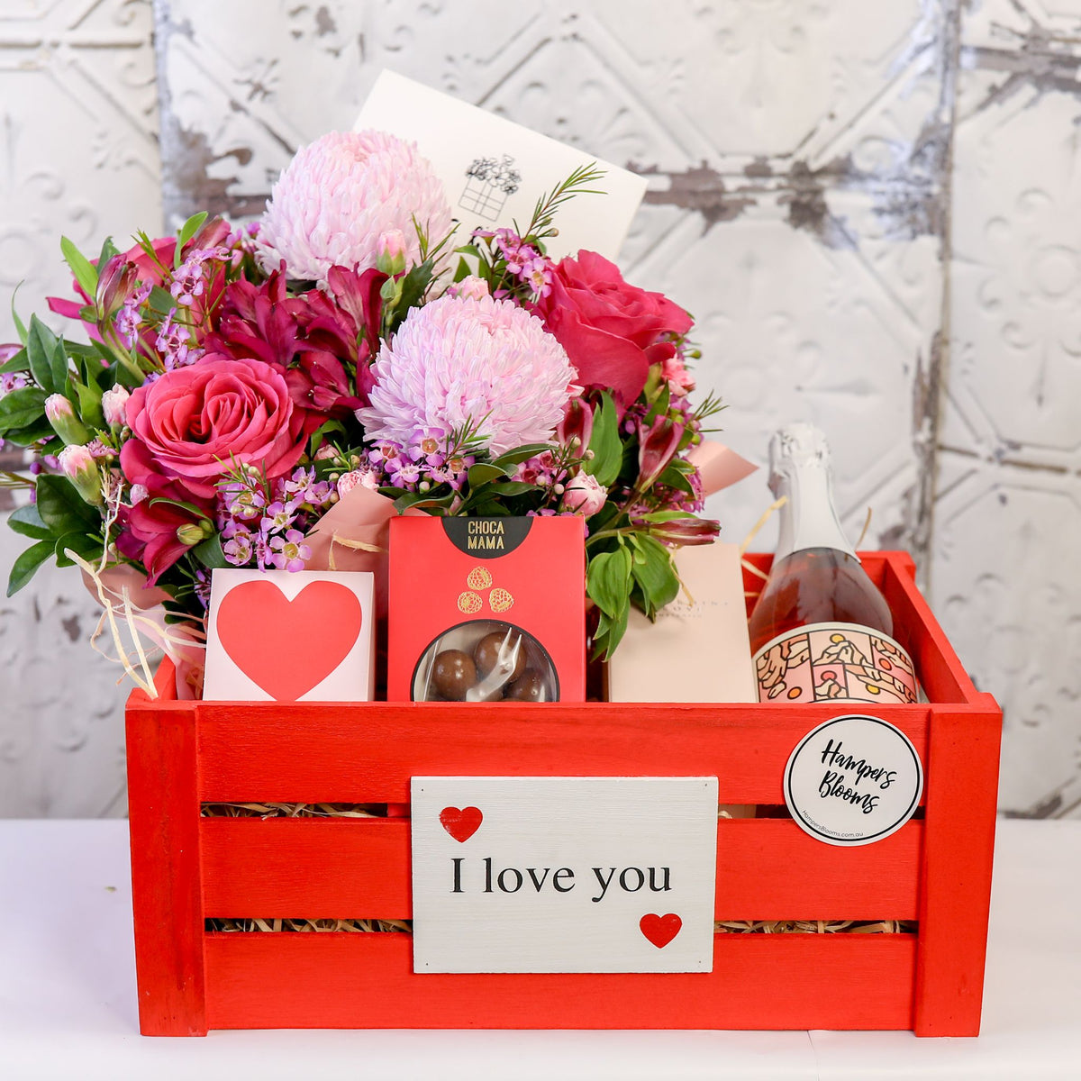Front view of pink flowers and gift packages above the front of a large red I love you crate