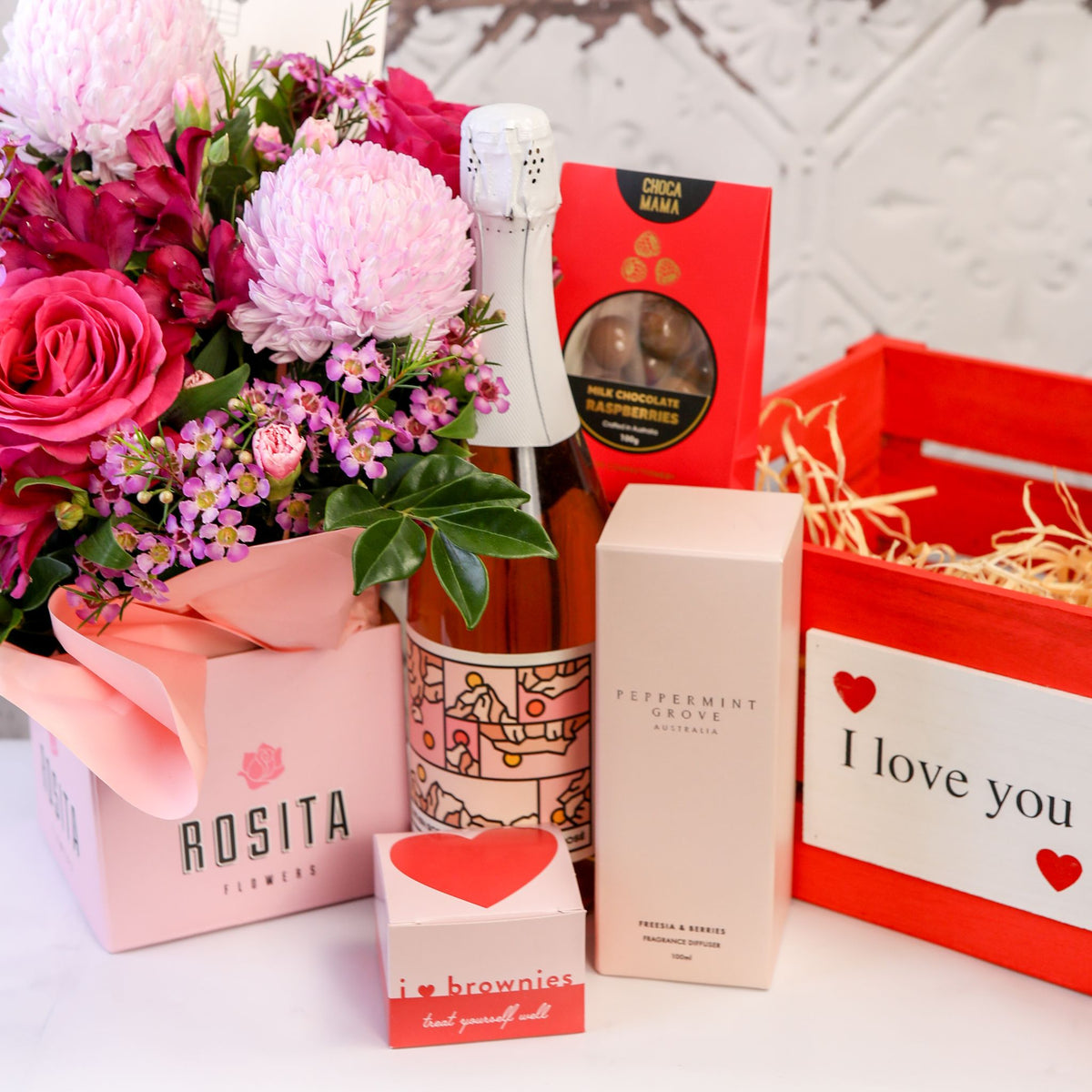 Pink floral pot, bottle, diffuser box and treats displayed beside a red I love you crate