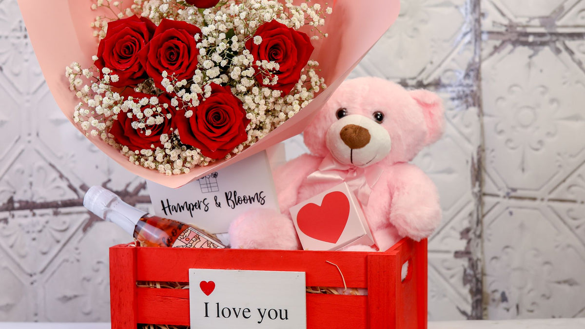 Landscape crop of red roses and pink teddy above the front of a red I love you crate