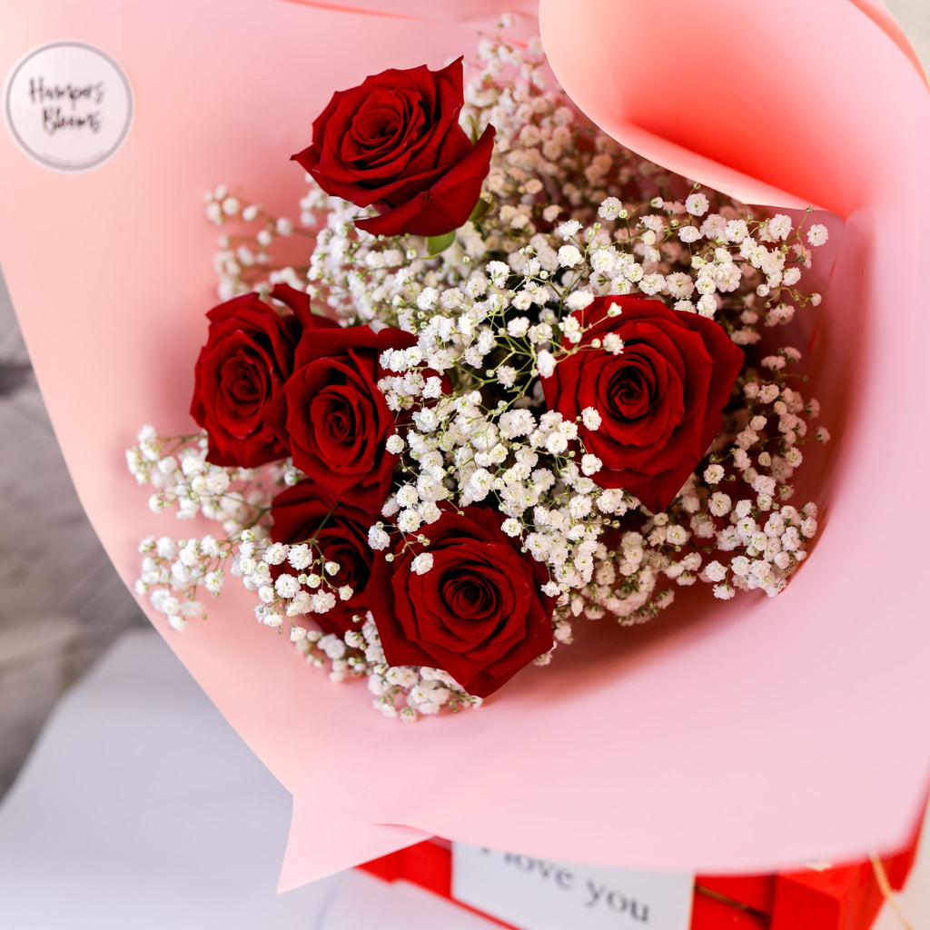 Tight detail of red roses and white filler flowers surrounded by pink wrapping