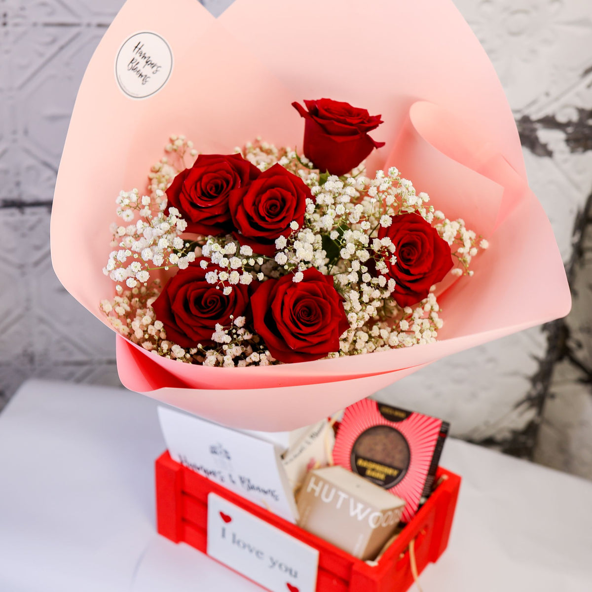 View from above of red roses and white filler flowers over chocolates and a candle box in a red crate