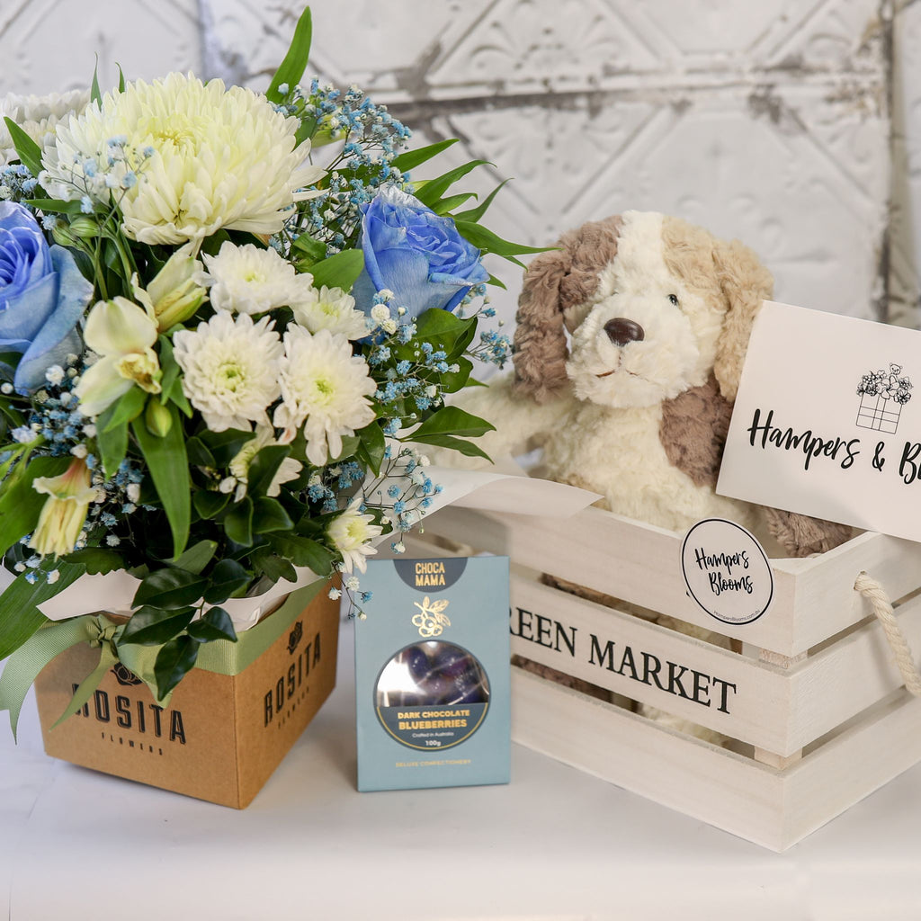 Blue and white floral pot and chocolate box beside a white crate holding a plush puppy and message card