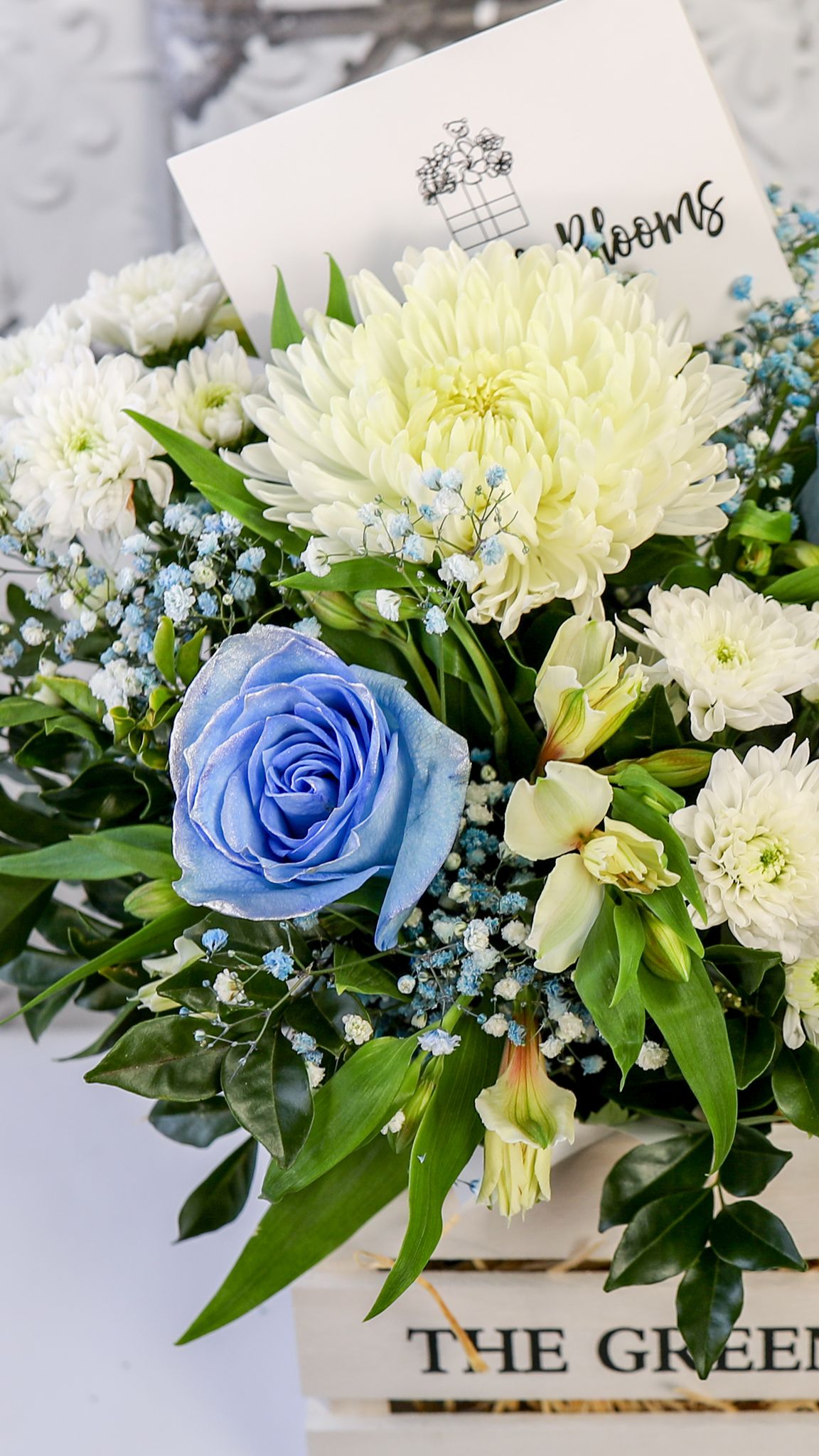 Tight portrait detail of blue-tinted roses, white blooms and foliage above the edge of a white crate