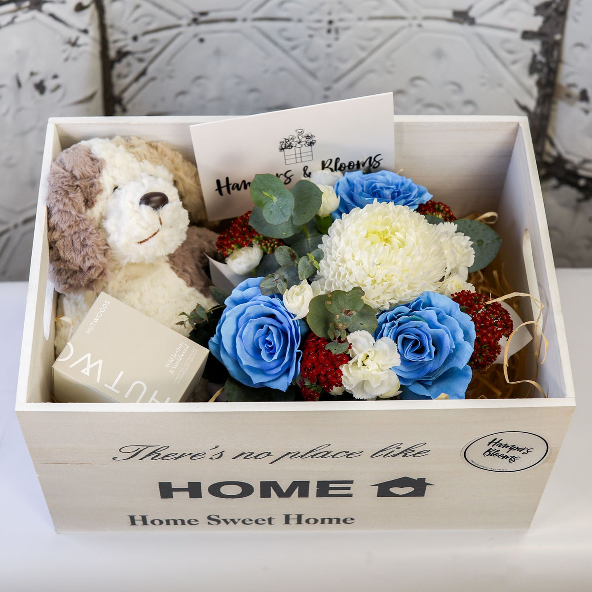 Close-up from above of blue-tinted roses, white blooms, plush puppy and candle box inside a white chest