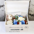Open white keepsake chest with blue-tinted roses, white flowers, plush puppy and boxed candle inside