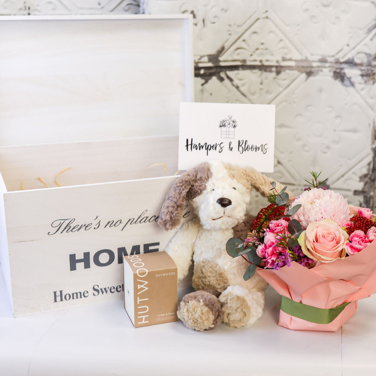 Pink floral pot, seated plush puppy and boxed candle displayed in front of an open white keepsake chest