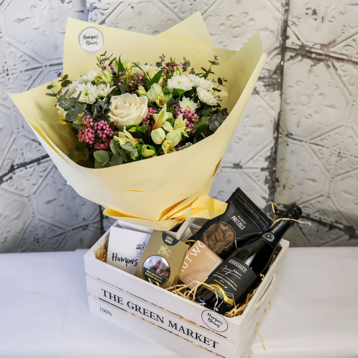 Angled view of a cream bouquet, sparkling bottle, chocolates and candle box in a white crate