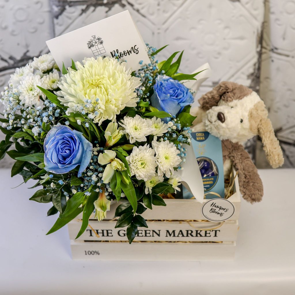 Blue-tinted flowers, plush puppy and chocolates in a crate